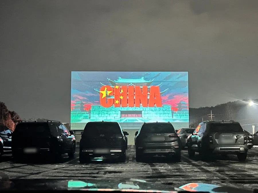 주차된 차량 너머로 대형 스크린의 영화를 관람하는 모습