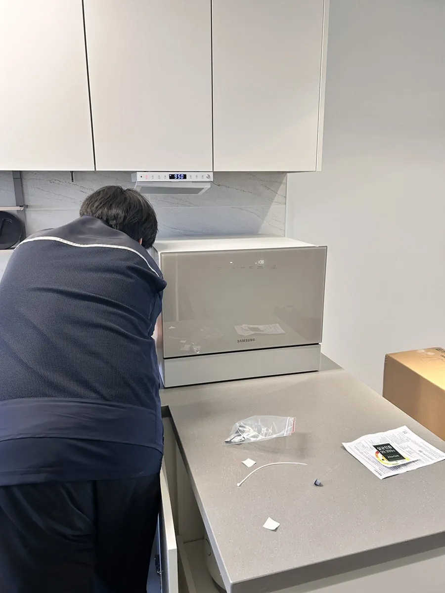 주방 조리대 위 식기세척기를 설치 중인 작업자